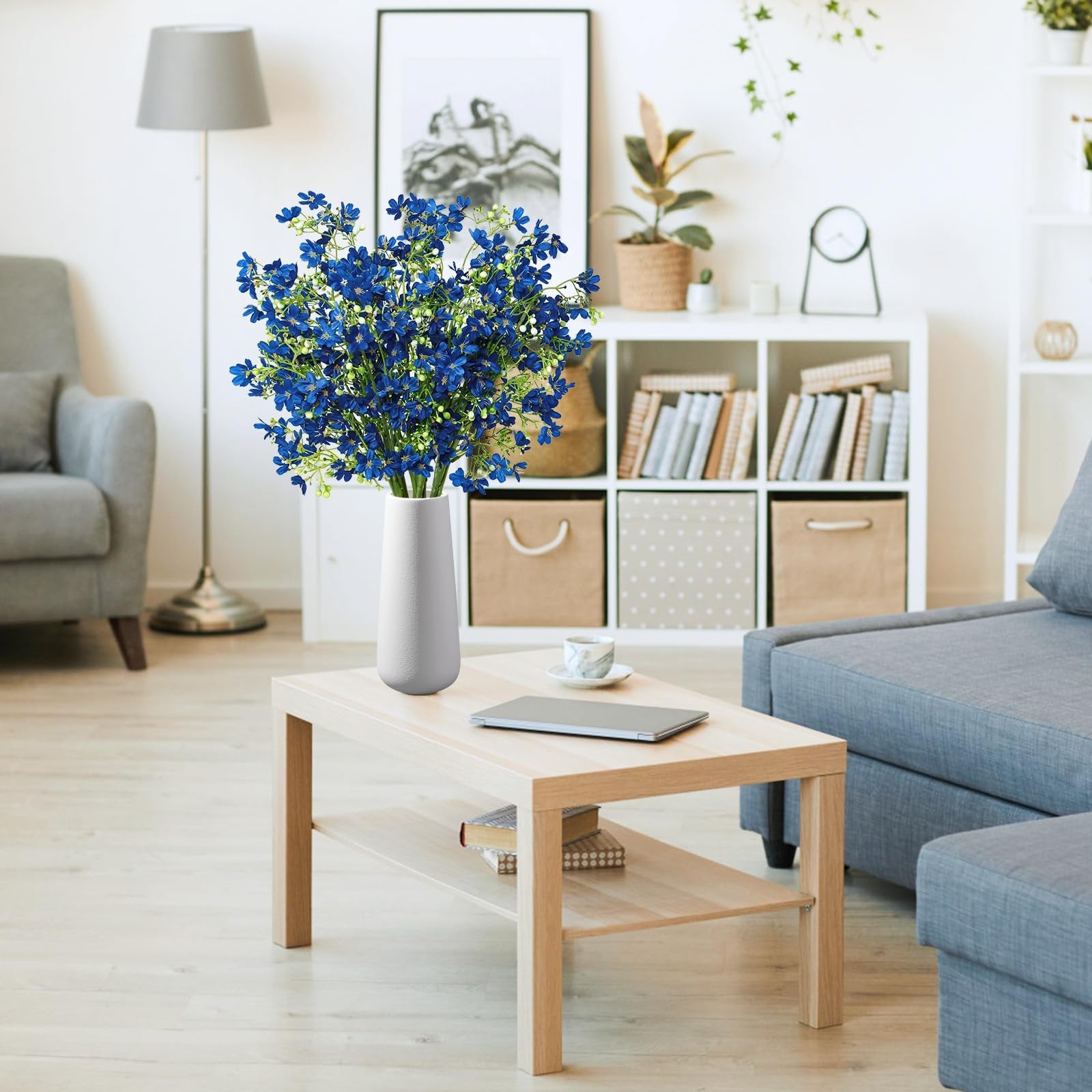 Blue baby's breath silk flowers in a white vase on a coffee table in a living room setting.
