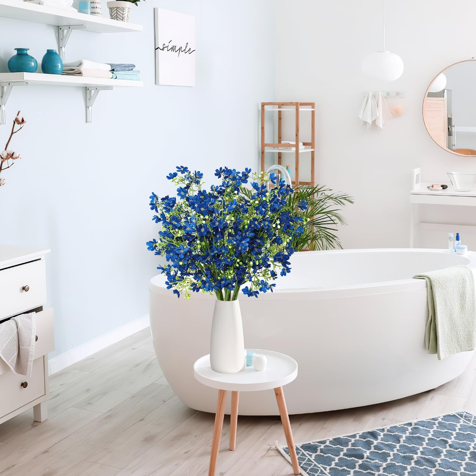 Blue baby's breath flowers in a white vase on a small table next to a bathtub.