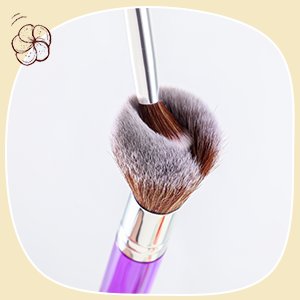 Purple handled makeup brushes with fluffy bristles, one brush inside another.