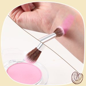 Close-up of a makeup brush applying pink powder to a wrist, with a pink powder compact in the foreground.
