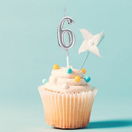 Silver number 6 birthday candle on a cupcake with white frosting and colorful sprinkles, against a light blue background.