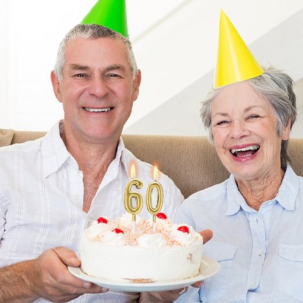 Elderly couple celebrating with a birthday cake topped with gold numeral candles showing '60'
