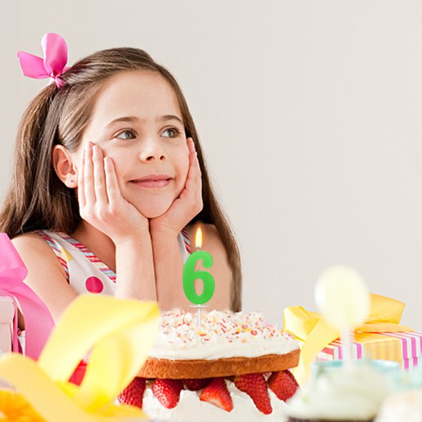 Girl with hands on cheeks looking at a birthday cake with a green number 6 candle lit