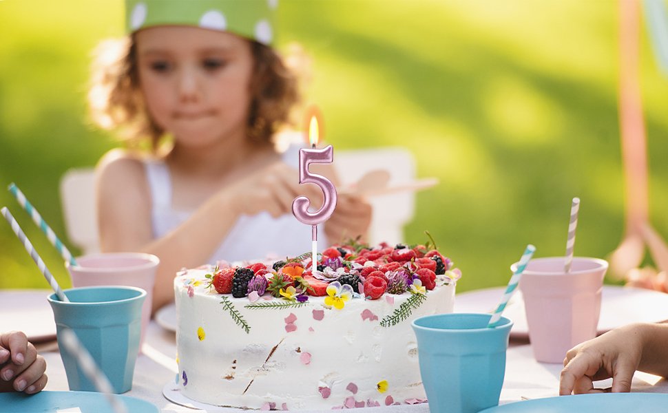 Birthday cake with a lit number 5 candle and berries, with a child in the background at an outdoor party.