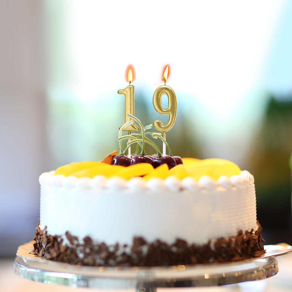 Gold numeral birthday candles '19' on a decorated cake with fruit and cherries.