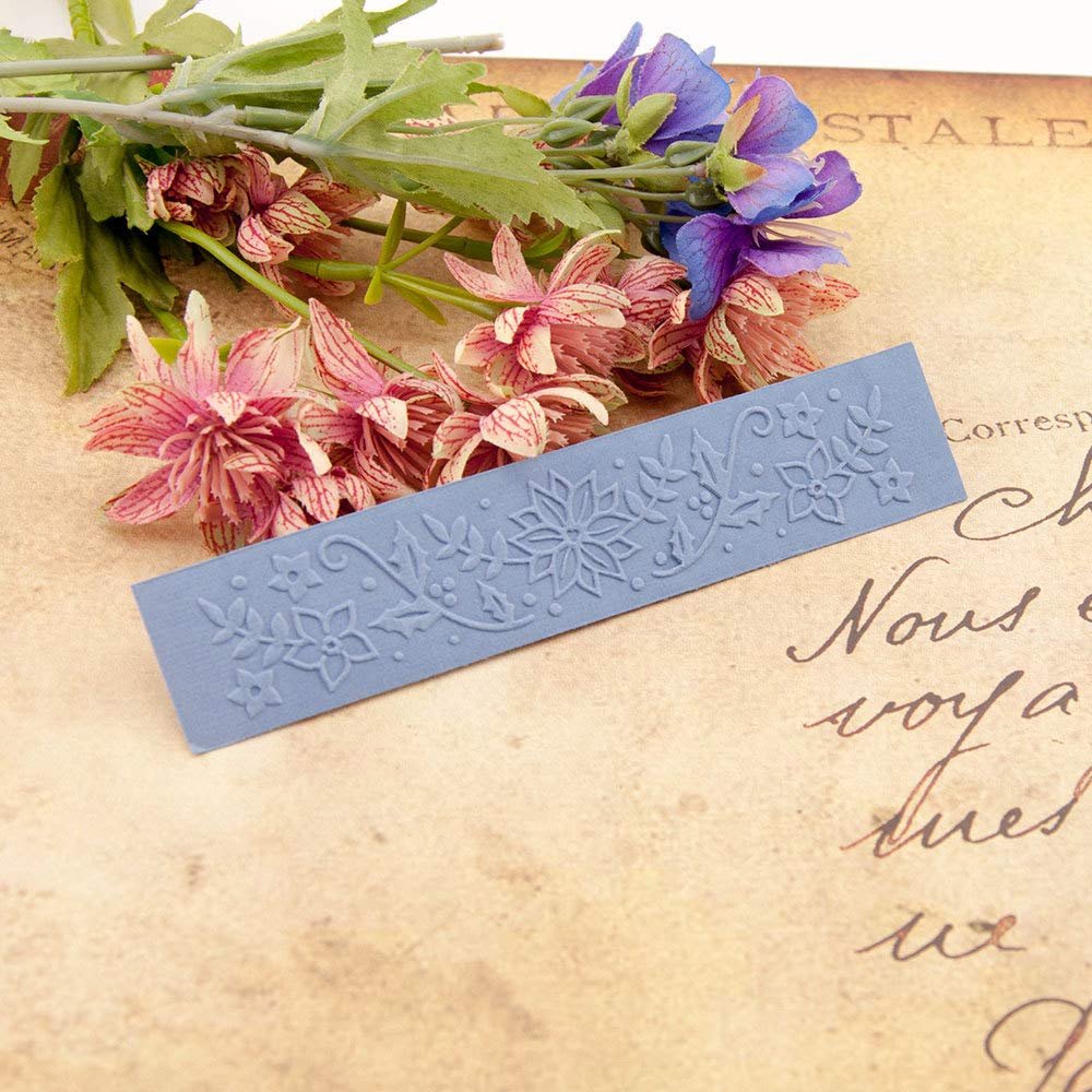 Blue plastic embossing folder with floral and leaf pattern, surrounded by artificial flowers and aged paper.