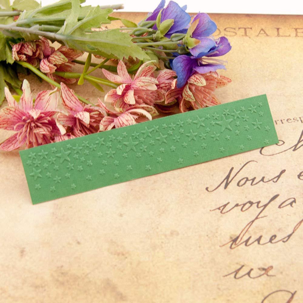 Green plastic embossing folder with star pattern, displayed with artificial flowers on vintage paper.