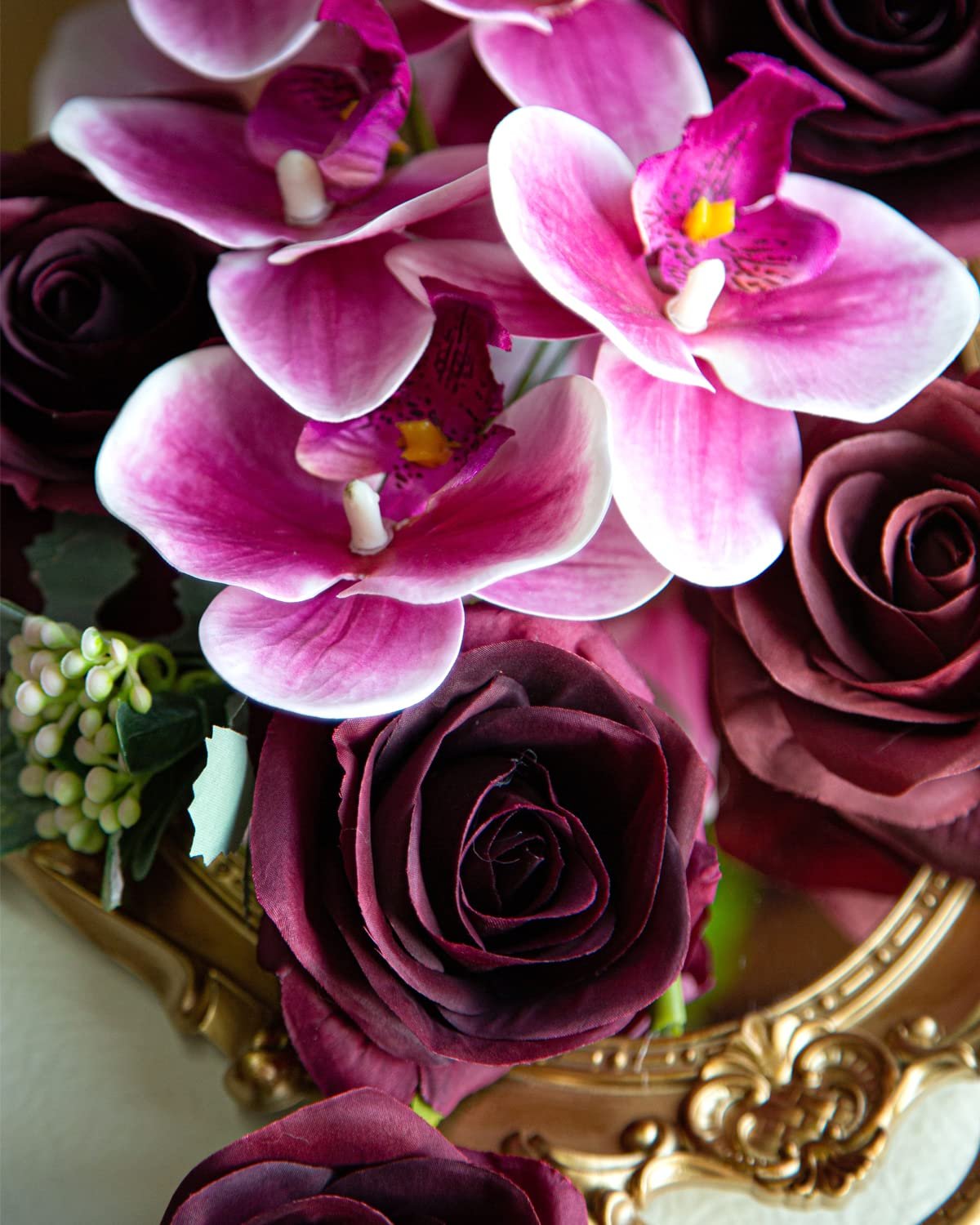 Burgundy silk roses and pink orchids arranged in a gold ornate vase.
