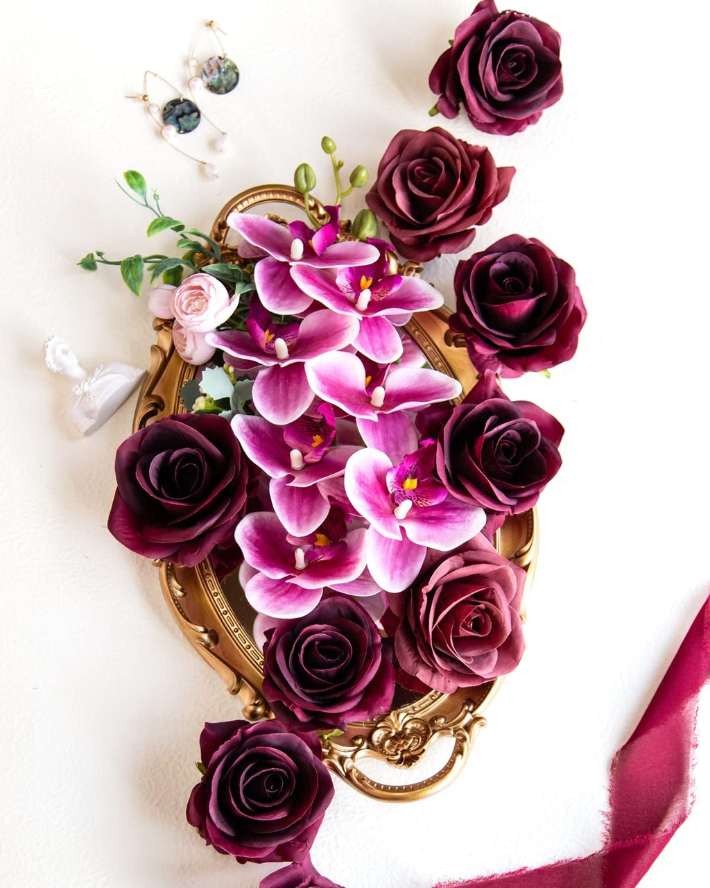 Burgundy silk roses and pink orchids arranged on a gold ornate tray with earrings and a ribbon