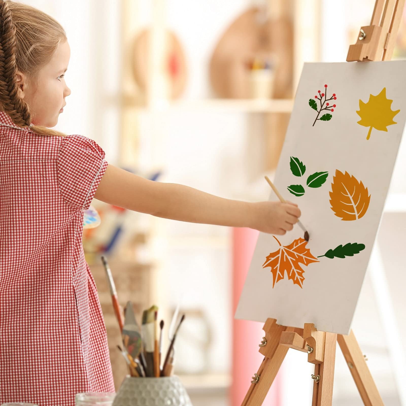 Young girl painting autumn leaf stencils on an easel with a brush