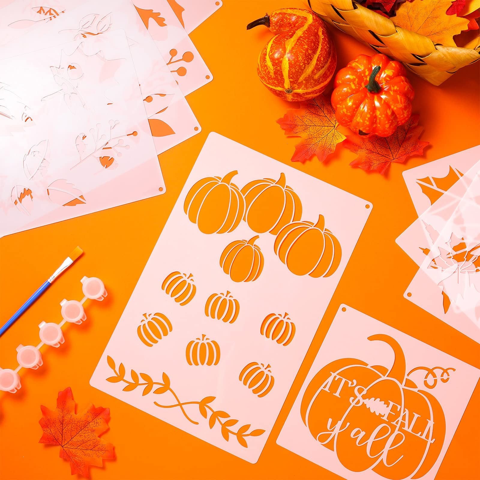 Thanksgiving stencils with pumpkin and leaf designs, paint brush, and paint pots on orange background