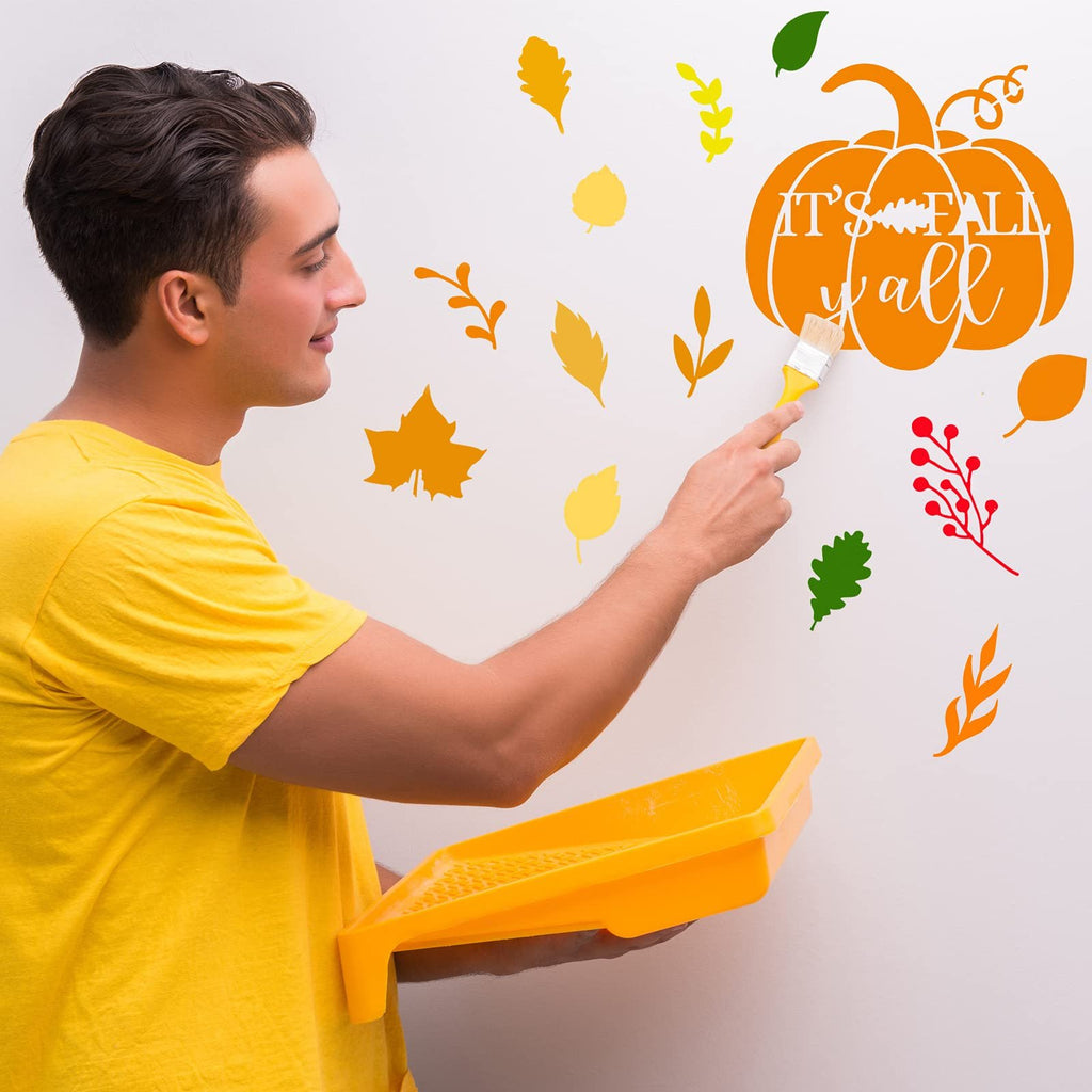 Man in yellow shirt painting autumn leaf and pumpkin stencils on a white wall with a brush and paint tray