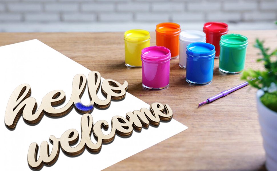 Wooden 'hello' and 'welcome' cutouts with jars of paint and a brush on a wooden table
