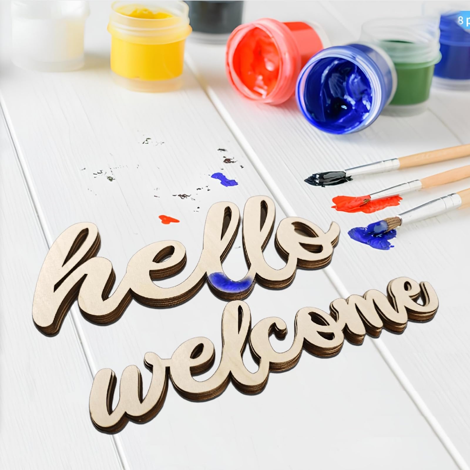 Wooden 'hello' and 'welcome' cutouts with paint and brushes on a white wooden surface
