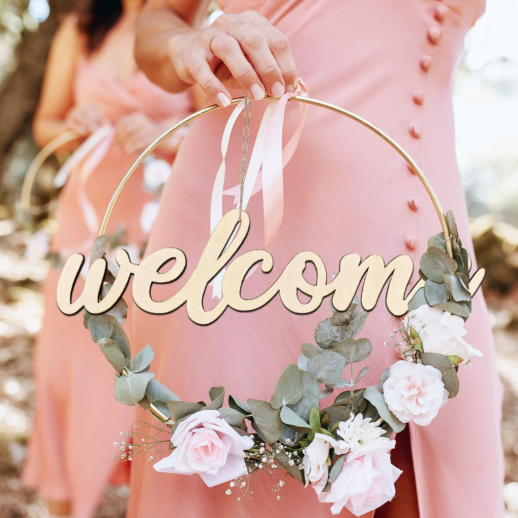 Woman holding a gold hoop wreath decorated with flowers and the word 'welcome' in wooden letters.