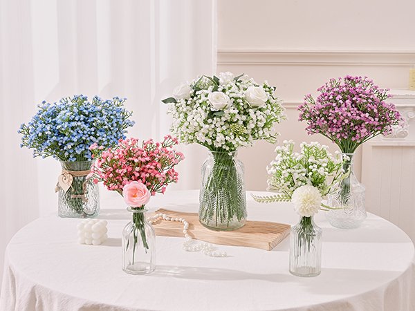 Assortment of artificial baby's breath flowers in various colors displayed in glass vases on a table.