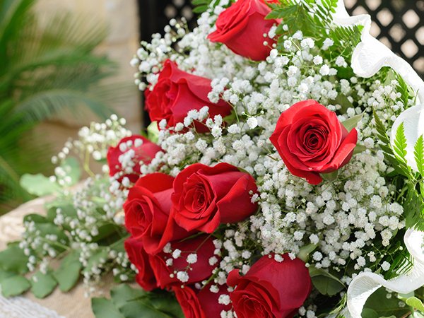 Close-up of a bouquet of red roses and white baby's breath flowers, arranged with greenery and white ribbon.