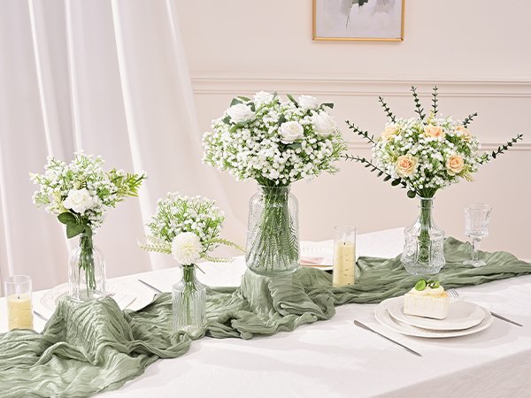 Four bouquets of artificial baby's breath and roses in glass vases on a table with a green runner