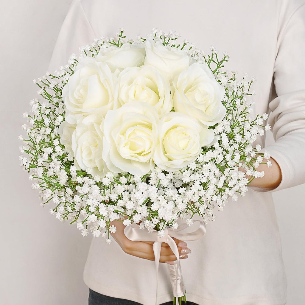 White artificial rose and baby's breath bouquet held by a person, tied with a satin ribbon.