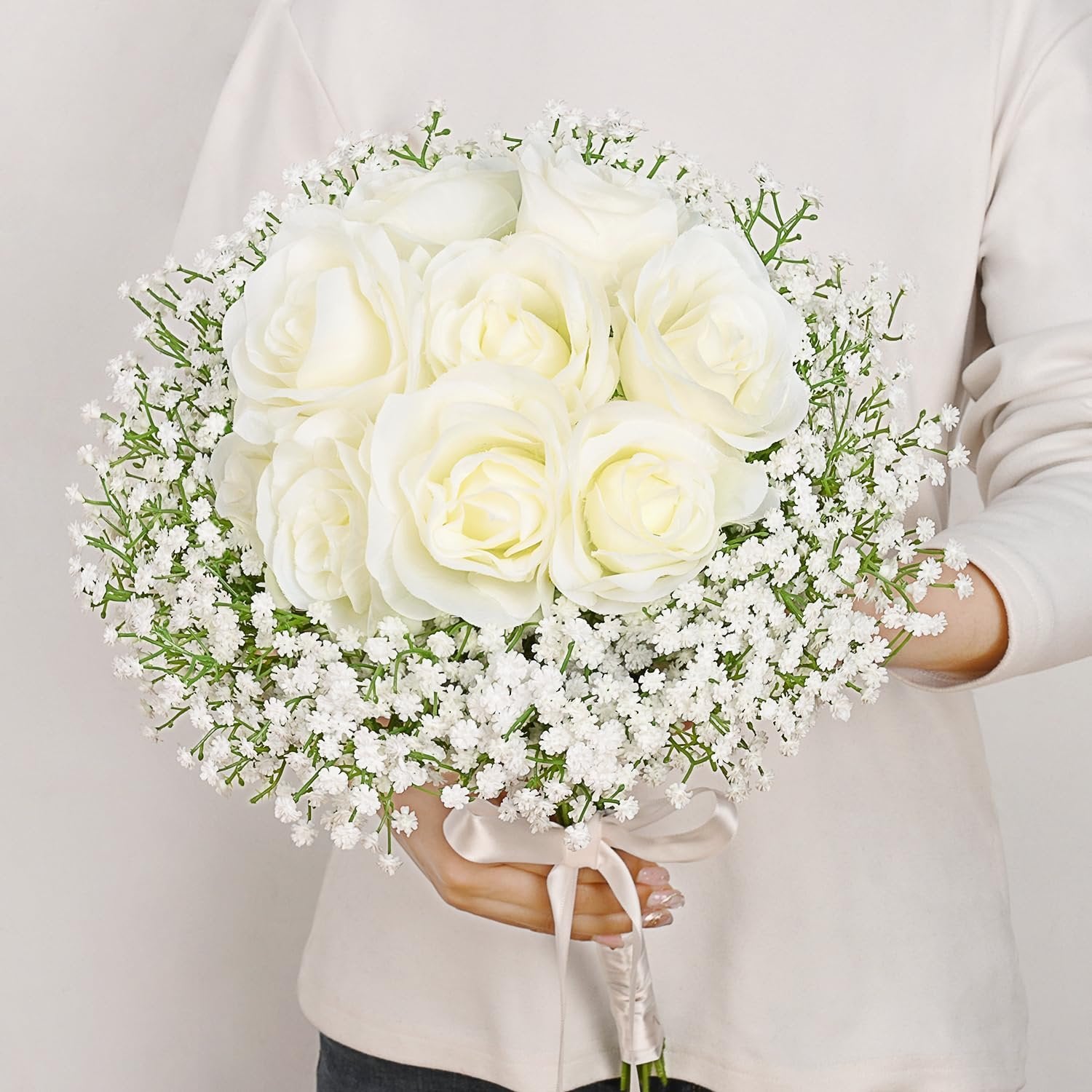White artificial rose and baby's breath bouquet held by a person, tied with a satin ribbon.
