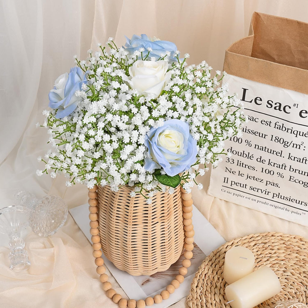 Artificial baby's breath and roses in a woven basket with wooden beads, next to candles and a paper bag.