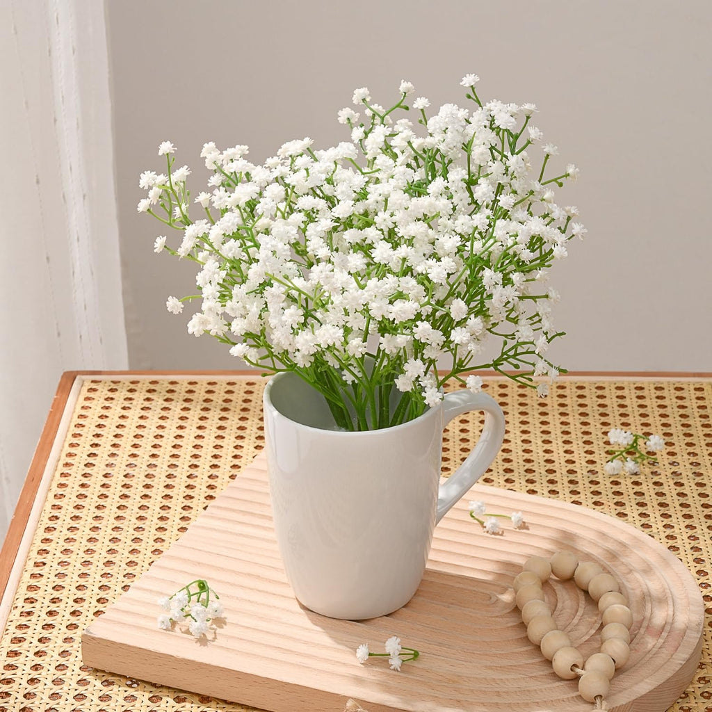 White artificial baby's breath flowers in a white mug on a wooden tray with beaded garland.