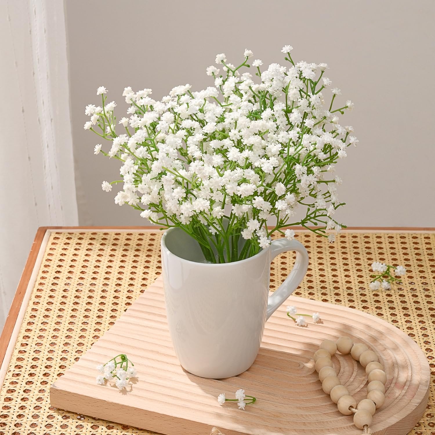 White artificial baby's breath flowers in a white mug on a wooden tray with beaded garland.