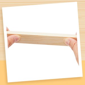 Hands holding a thin wooden rolling pin guide strip, demonstrating thickness