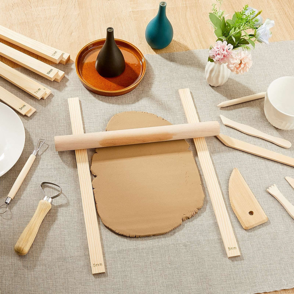 Clay rolling pin guides and tools arranged on a table with clay and decorative vases.