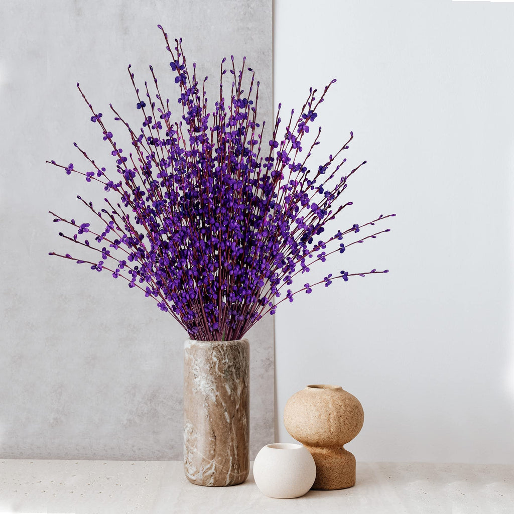 Bouquet of dark purple artificial jasmine flowers in a marble vase with two decorative vases on the side.
