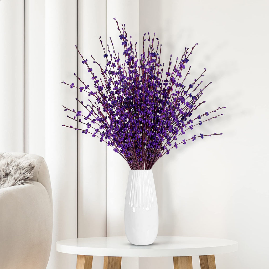 Artificial dark purple jasmine flowers in a white vase on a table next to a sofa.
