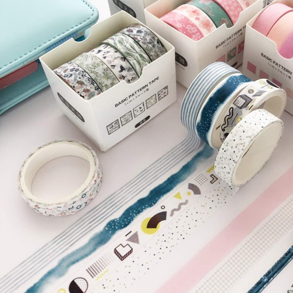 Several rolls of decorative washi tape with various patterns, including floral, geometric, and watercolor designs, displayed on a white surface next to a light blue organizer.