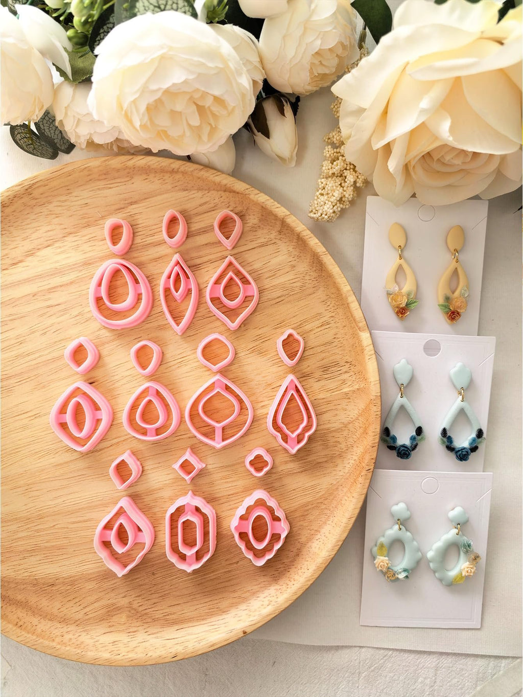 Set of pink polymer clay earring cutters in various shapes on a wooden plate, with finished earrings displayed to the right.