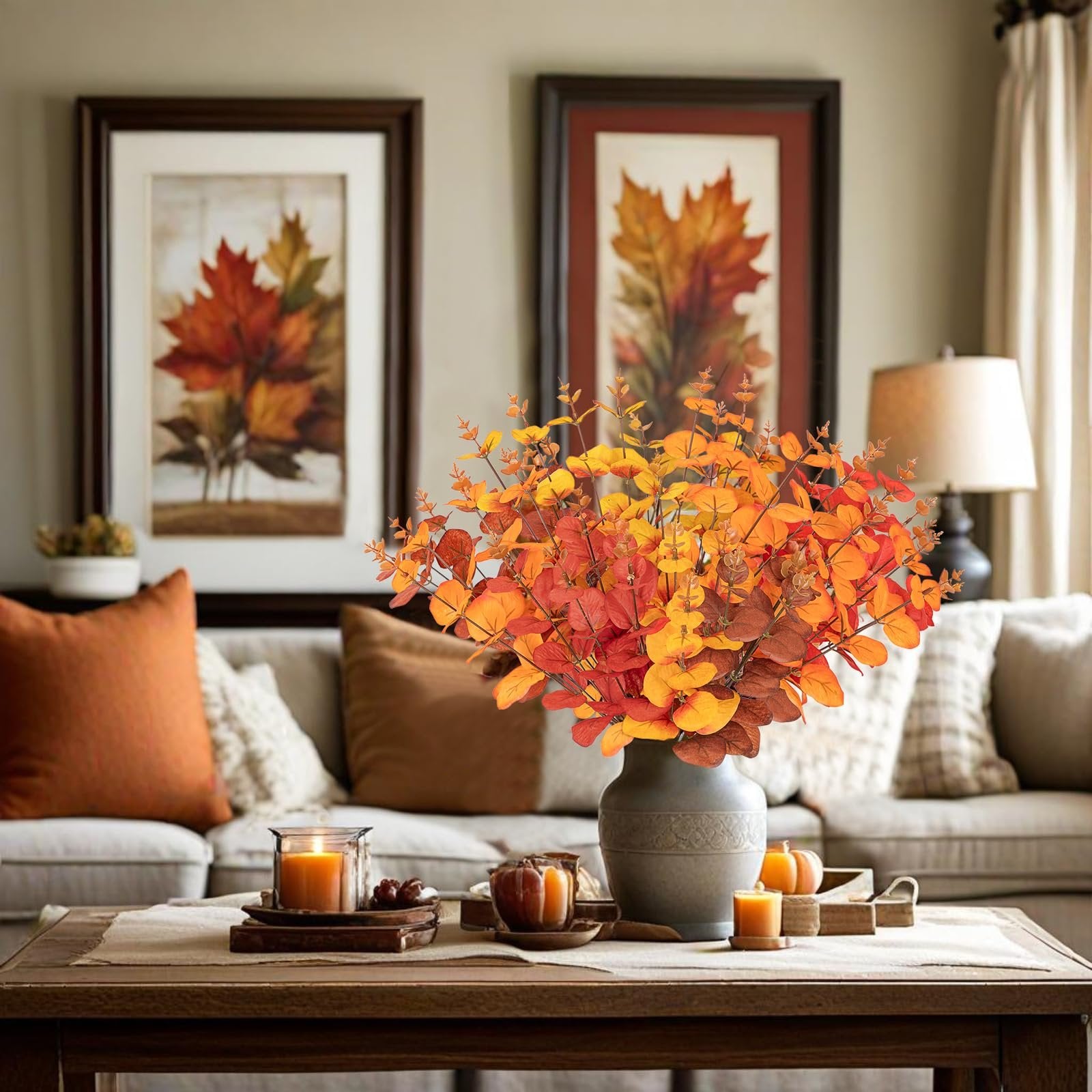 Fall eucalyptus bouquet in orange, red, and yellow hues arranged in a vase on a coffee table with candles and pumpkins.