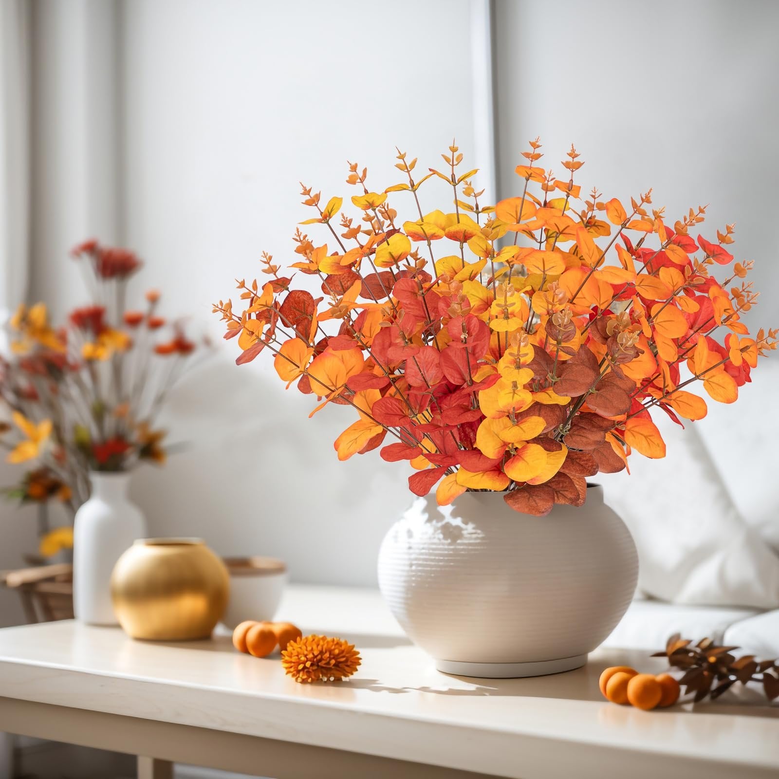 Artificial eucalyptus bouquet in fall colors of orange, red, and yellow, displayed in a white vase on a table.