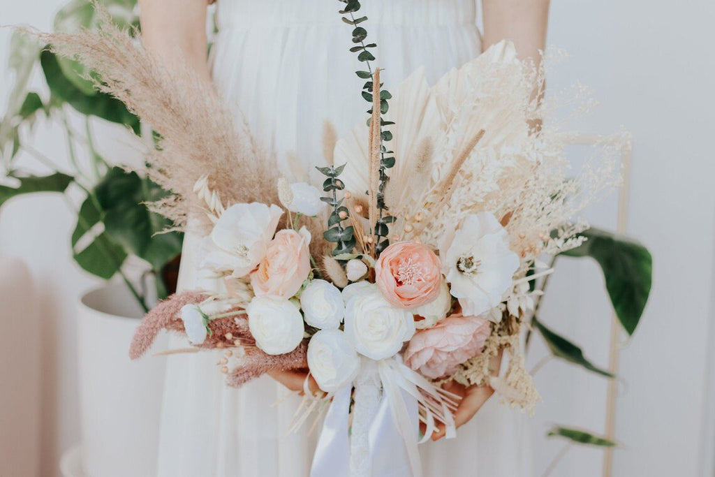 Bride holding a bouquet of dried flowers including eucalyptus, pampas grass, and roses.