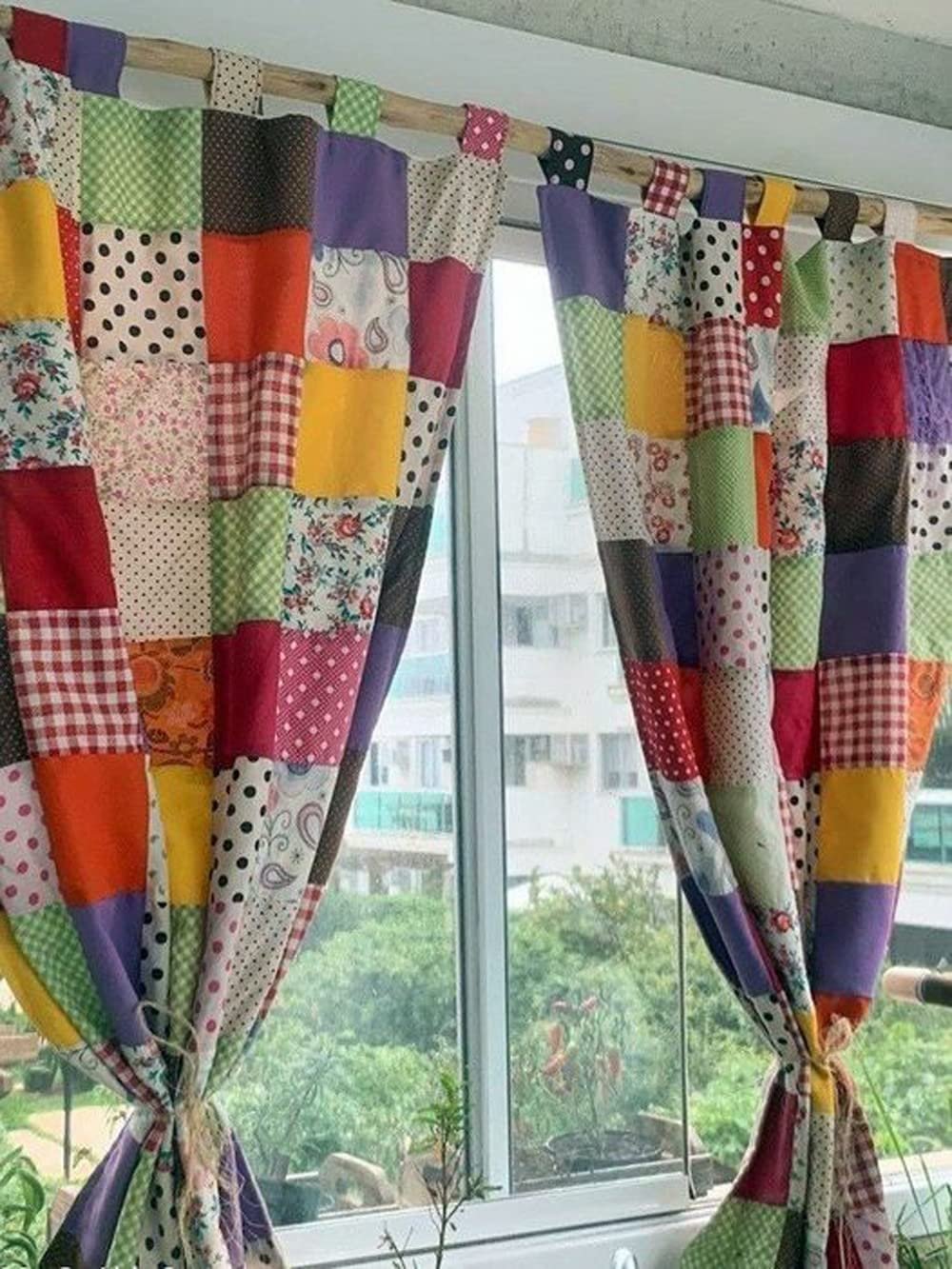 Patchwork curtains made of colorful fabric squares hanging on a window rod, tied with twine.