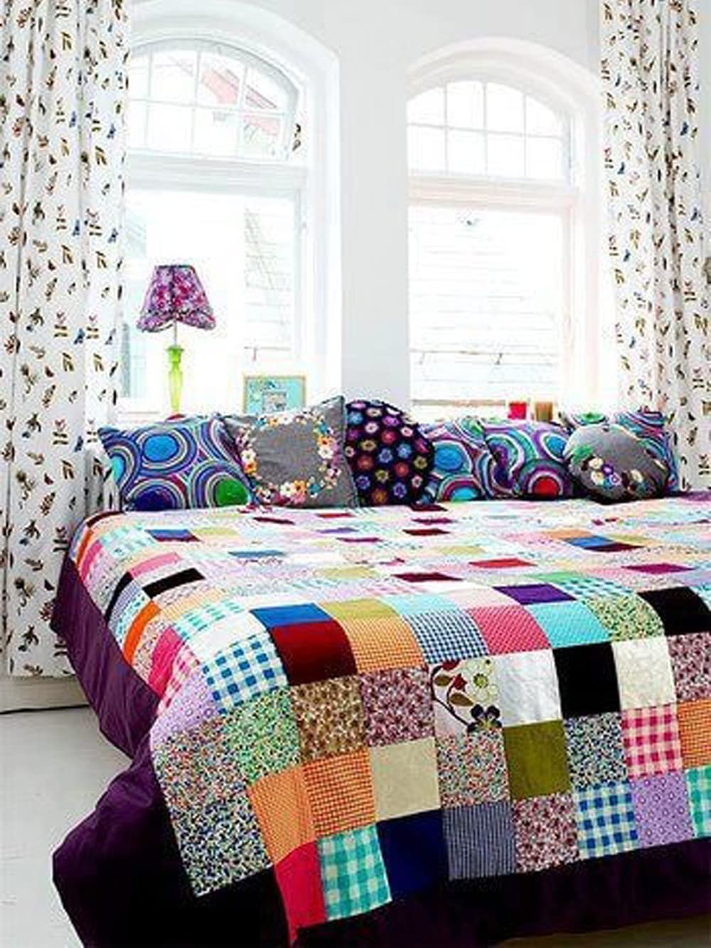 Colorful patchwork quilt on a bed with decorative pillows and patterned curtains.