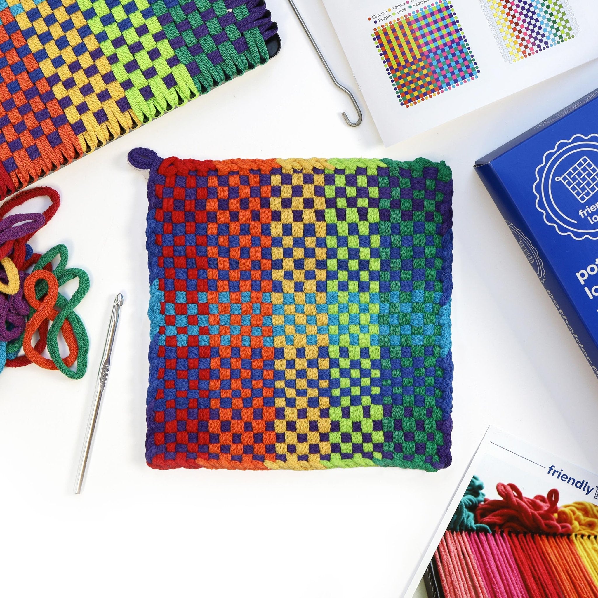 Potholder weaving kit with rainbow loops, crochet hook, and instruction booklet on white background