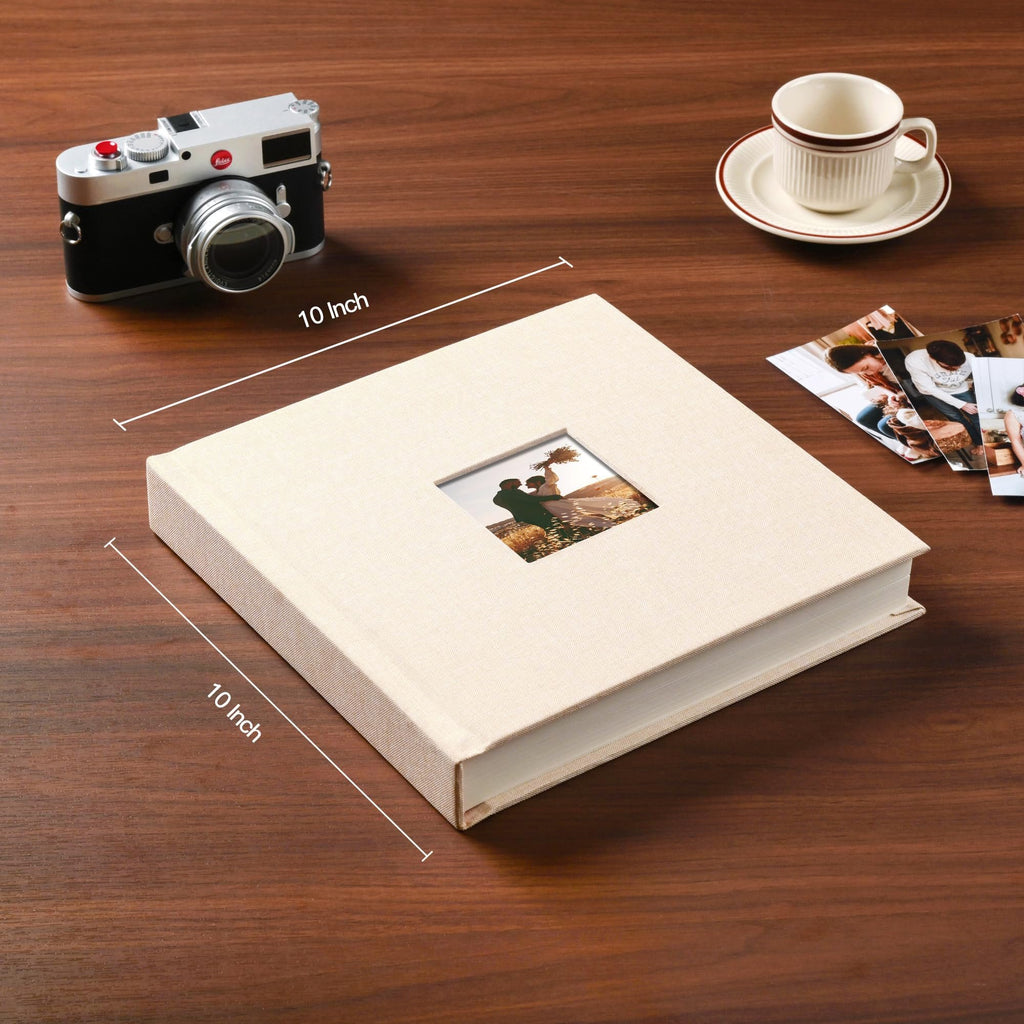 Beige linen hardcover scrapbook album with a photo frame on the cover, shown on a wooden table with a vintage camera and photos.