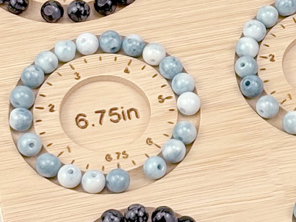 Bamboo beading board with bracelets made of light blue and white beads, showing measurement markings and a 6.75 inch diameter circle.