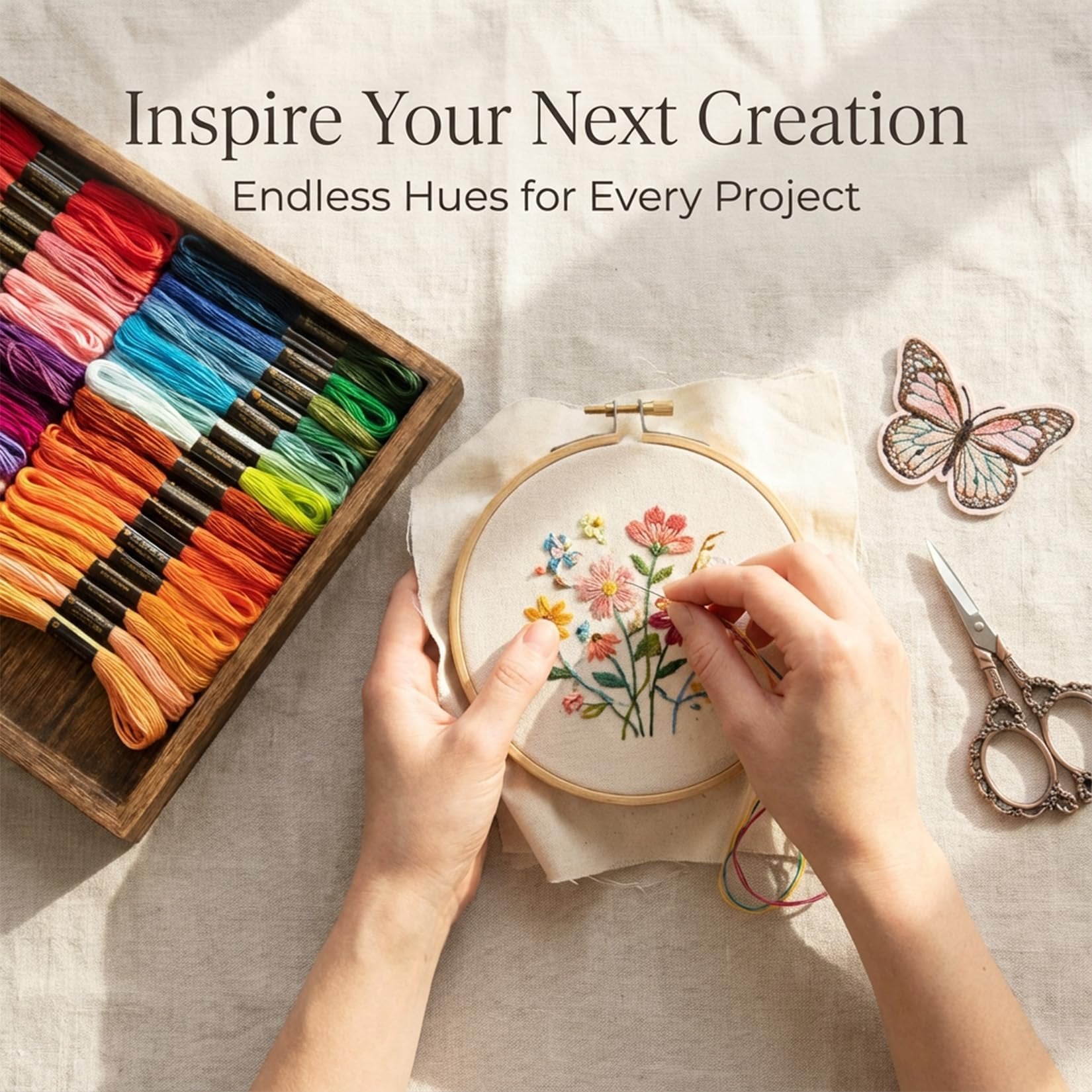 Hands embroidering a floral design with colorful threads and a wooden hoop, next to a tray of embroidery floss and scissors.