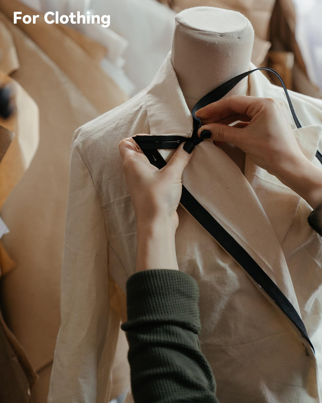 Hands pinning black ribbon to a cream-colored fabric draped over a mannequin, with 'For Clothing' overlay.