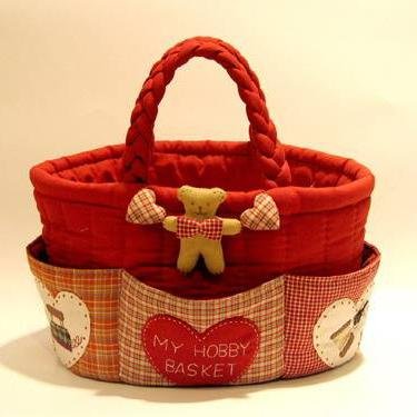 Red fabric hobby basket with braided handle, decorated with a teddy bear and hearts, featuring multiple pockets with assorted prints.