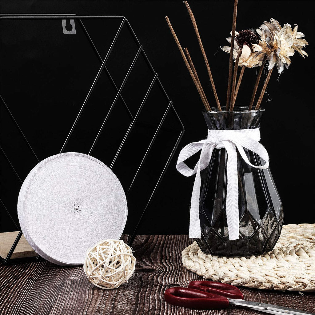 Roll of white cotton twill tape ribbon with herringbone weave, next to a vase with dried flowers and scissors on a wooden surface.