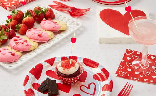 Bamboo cocktail picks with red heart tops in appetizers, cookies, and a cupcake on a table setting.