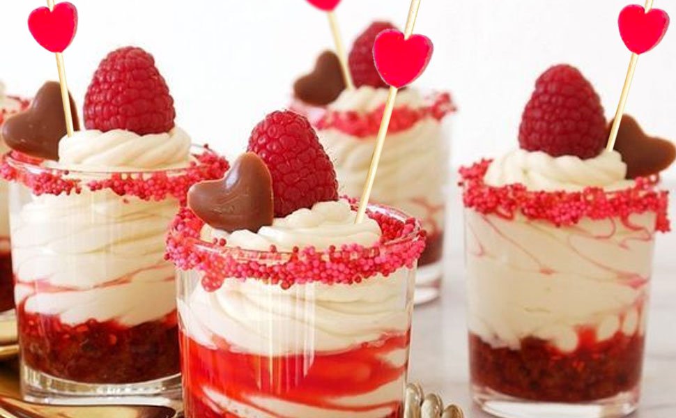 Dessert parfaits topped with raspberries and chocolate hearts, decorated with red sprinkles and heart-shaped bamboo cocktail picks.
