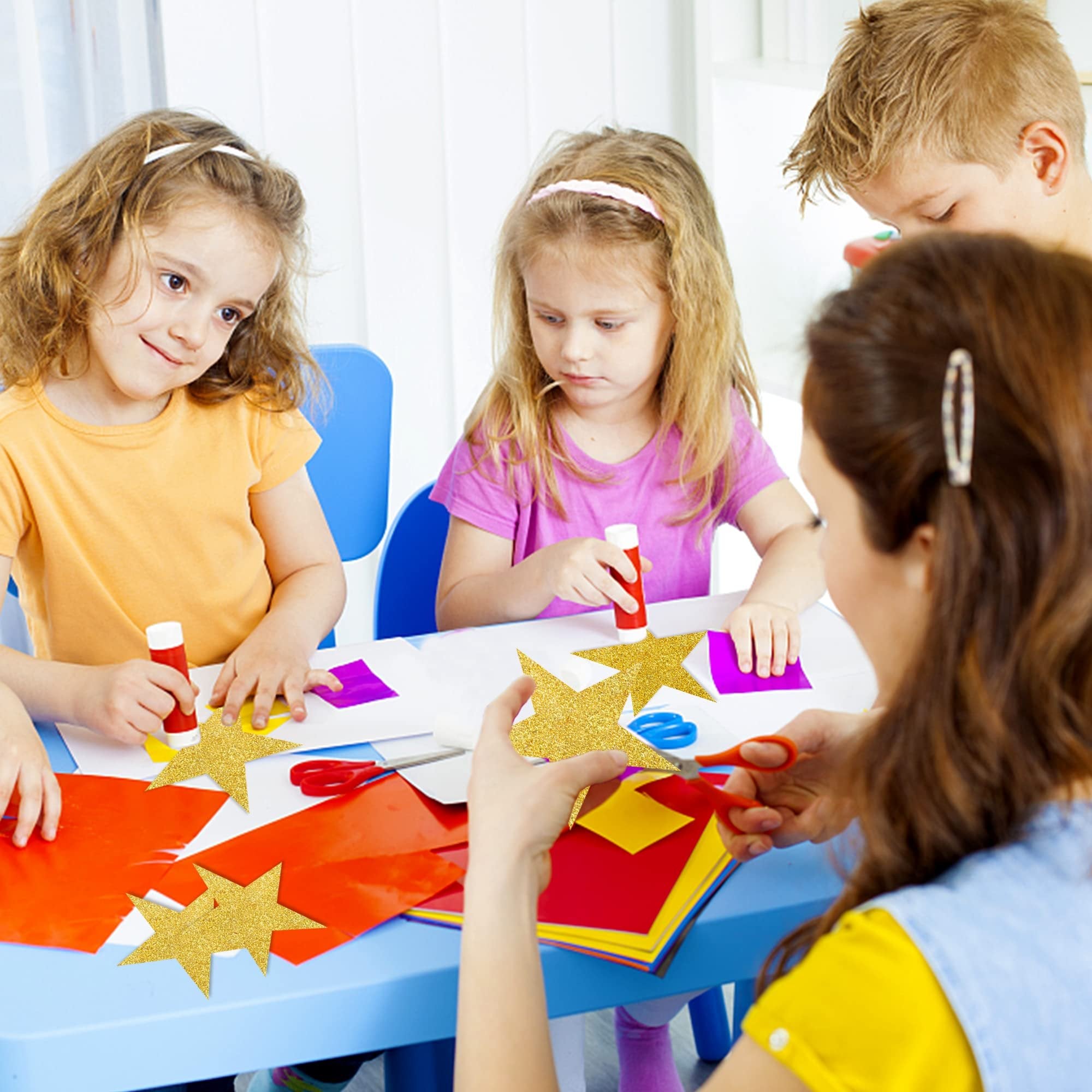 Children and adult crafting with glitter gold star cutouts and colorful paper at a table