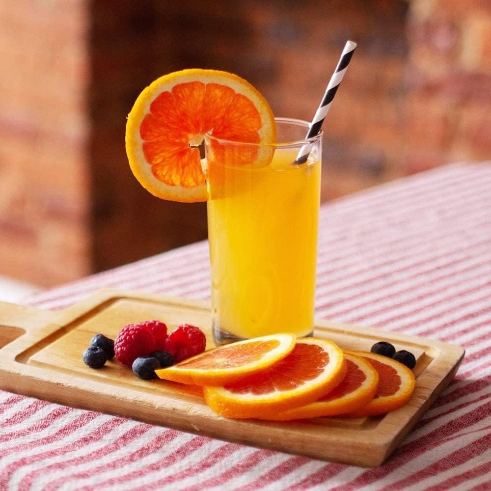 Glass of orange juice with a straw and orange slice garnish, served with berries on a wooden board.