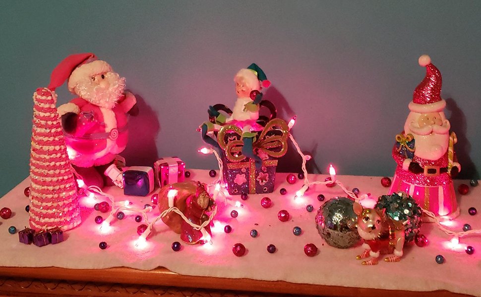 Christmas display with pink string lights, Santa figures, and festive ornaments on a white surface.